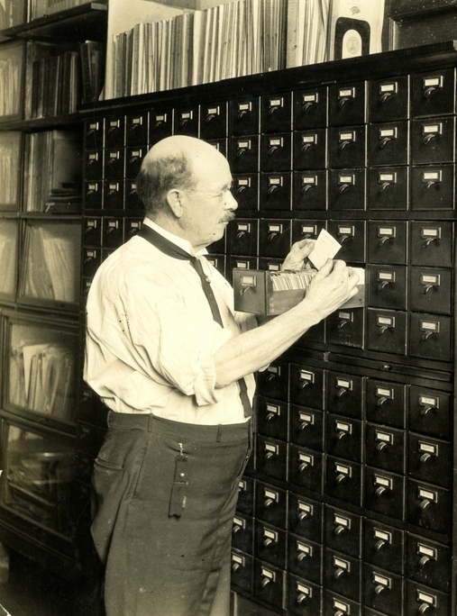 Photograph of Albert Hassal going through the drawer of a card catalog.