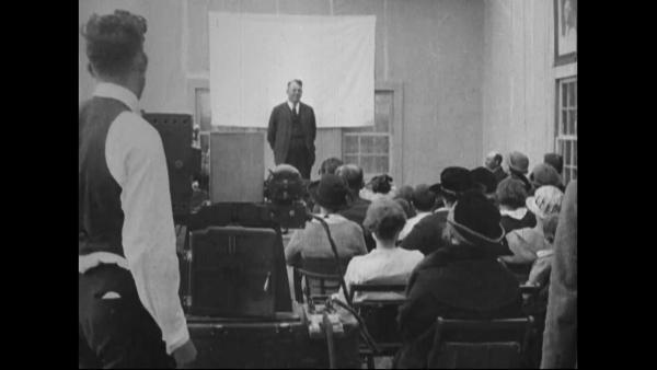 image of man standing in front of a crowd with a movie screen behind him