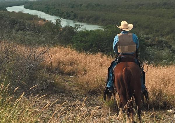 image of a man on a horse standing in a filed looking over water